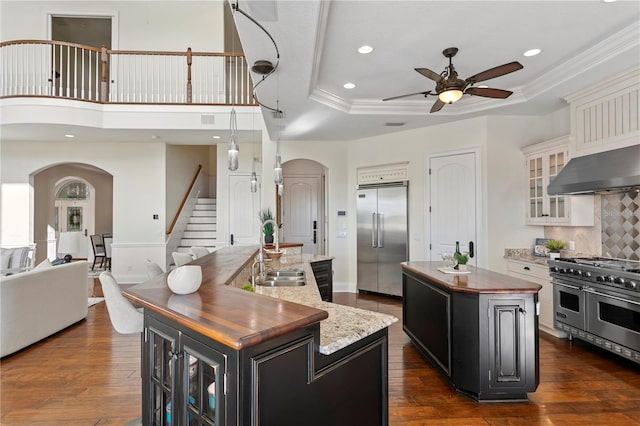 kitchen with a kitchen island with sink, high end appliances, arched walkways, and a sink