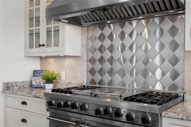 kitchen featuring glass insert cabinets, light stone counters, decorative backsplash, custom exhaust hood, and range