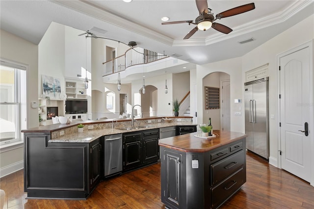 kitchen with visible vents, a tray ceiling, a large island with sink, a sink, and built in refrigerator