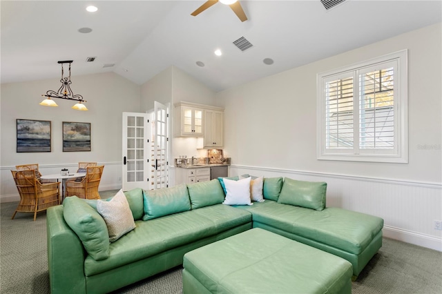 living area with visible vents, a wainscoted wall, vaulted ceiling, light carpet, and a ceiling fan