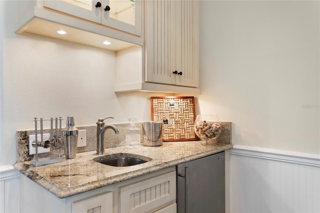 kitchen featuring glass insert cabinets, a wainscoted wall, light stone counters, fridge, and a sink