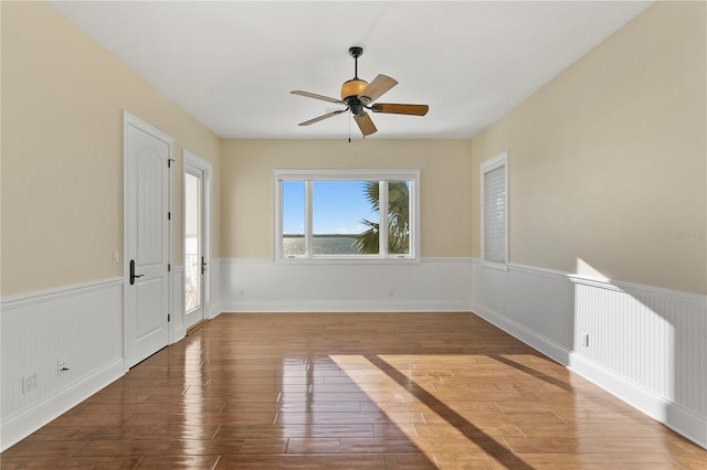 empty room featuring a wainscoted wall, wood finished floors, and ceiling fan