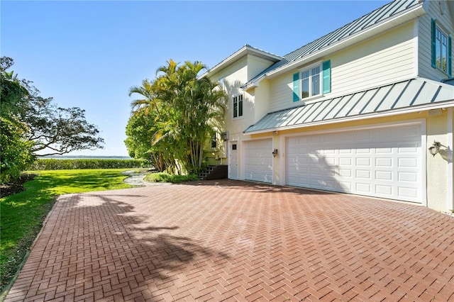 view of property exterior featuring stucco siding, metal roof, decorative driveway, a garage, and a standing seam roof