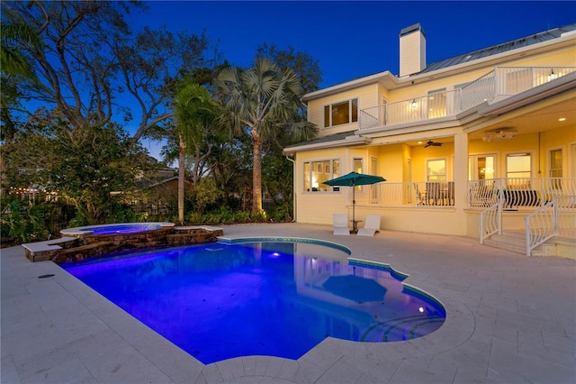 pool at night with a ceiling fan, a patio area, and a pool with connected hot tub