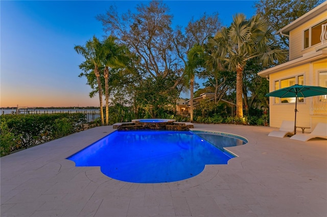 pool at dusk with a pool with connected hot tub and a patio