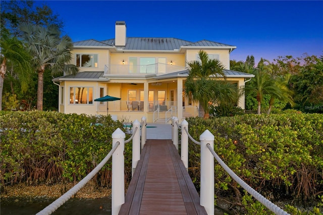 back of property with a standing seam roof, a balcony, a chimney, and metal roof