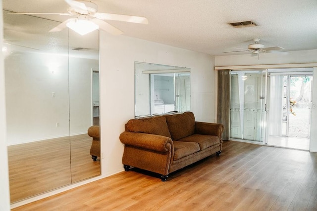 living area featuring ceiling fan, wood-type flooring, and a textured ceiling