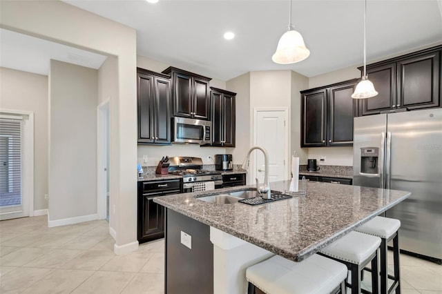 kitchen featuring sink, dark stone countertops, pendant lighting, stainless steel appliances, and a kitchen island with sink