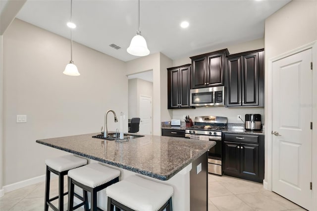 kitchen with appliances with stainless steel finishes, an island with sink, sink, dark stone counters, and hanging light fixtures