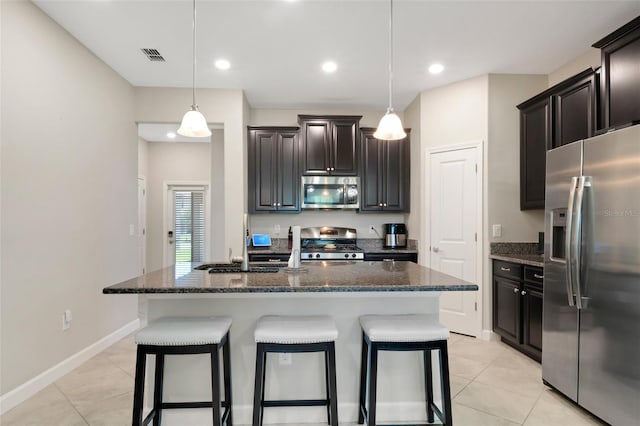 kitchen with stainless steel appliances, dark brown cabinets, a center island with sink, and decorative light fixtures