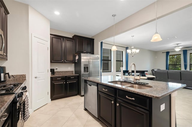 kitchen with appliances with stainless steel finishes, decorative light fixtures, sink, dark stone countertops, and a center island with sink