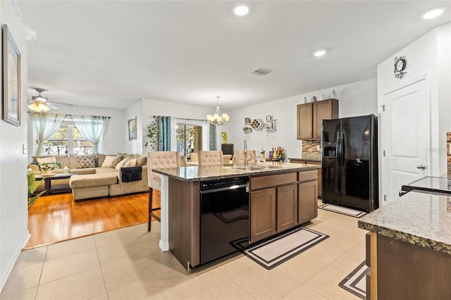 kitchen featuring sink, a breakfast bar area, a center island with sink, light tile patterned floors, and black appliances