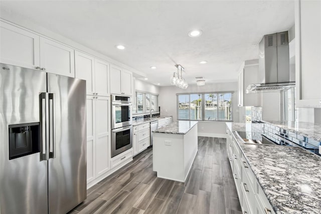 kitchen featuring a center island, dark wood finished floors, appliances with stainless steel finishes, white cabinetry, and wall chimney exhaust hood