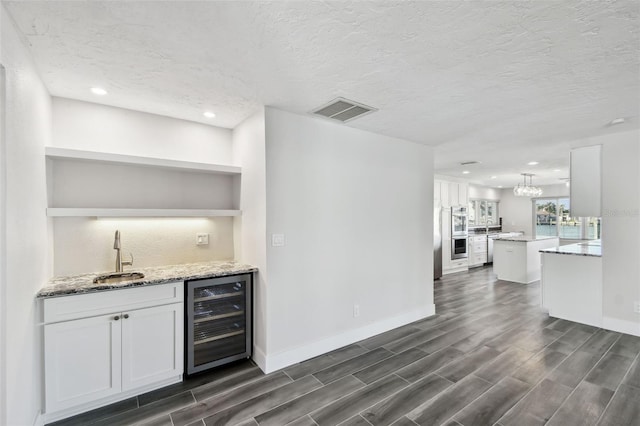 bar featuring beverage cooler, wood finish floors, a sink, visible vents, and indoor wet bar