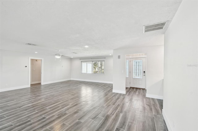 unfurnished living room featuring visible vents, a textured ceiling, baseboards, and wood finished floors