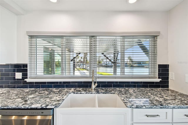 kitchen featuring stainless steel dishwasher, a sink, white cabinetry, and tasteful backsplash