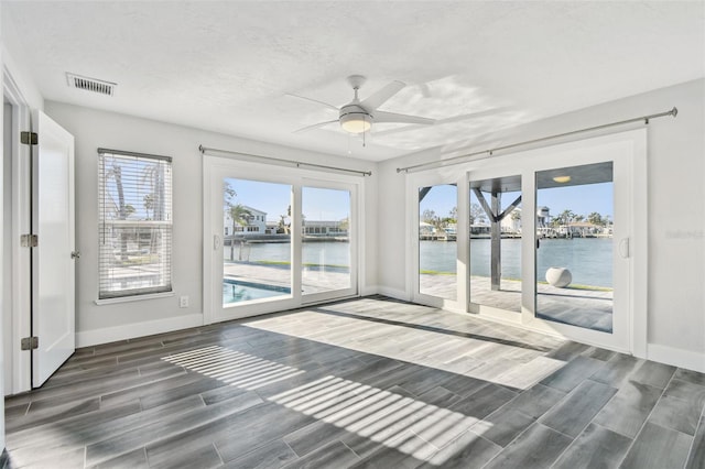 unfurnished sunroom featuring a water view, ceiling fan, and visible vents