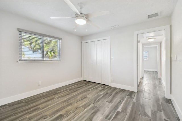 unfurnished bedroom with ceiling fan, wood finish floors, visible vents, baseboards, and a closet