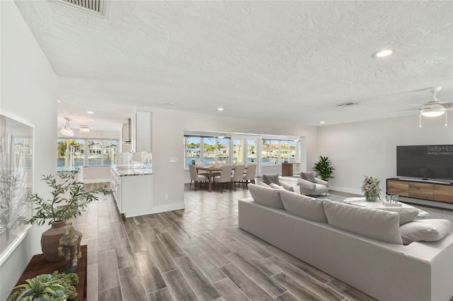 living room featuring a textured ceiling, wood finished floors, visible vents, and recessed lighting