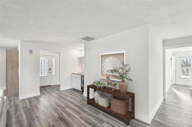 corridor featuring visible vents, a textured ceiling, baseboards, and wood finished floors