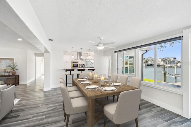 dining area with visible vents, a water view, wood tiled floor, a textured ceiling, and baseboards