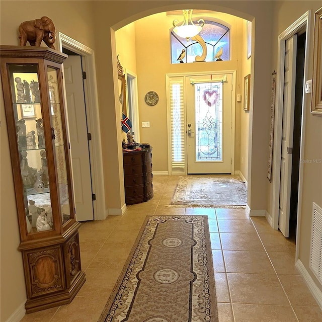 foyer entrance with visible vents, baseboards, arched walkways, and light tile patterned flooring