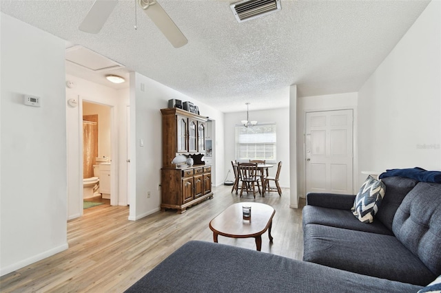 living room featuring ceiling fan with notable chandelier, light hardwood / wood-style floors, and a textured ceiling