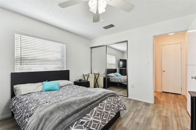 bedroom featuring ceiling fan, a textured ceiling, light hardwood / wood-style floors, and a closet