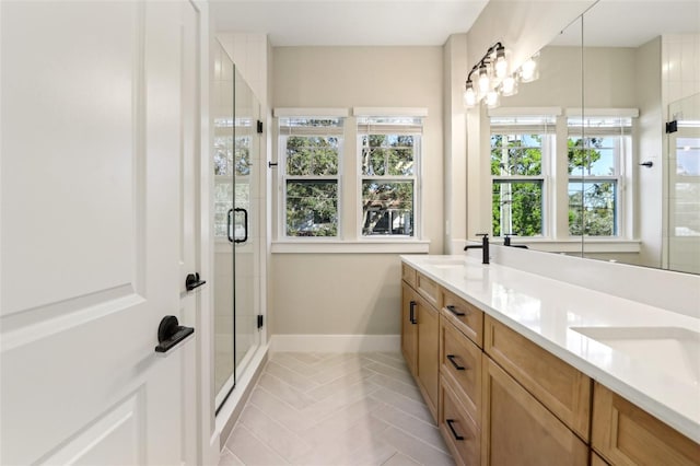 full bathroom with double vanity, a shower stall, baseboards, and a sink