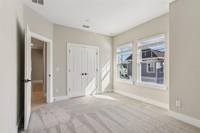 unfurnished bedroom with light carpet, a closet, visible vents, and baseboards