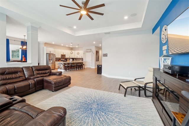 living room featuring decorative columns, ceiling fan, light hardwood / wood-style floors, and a tray ceiling