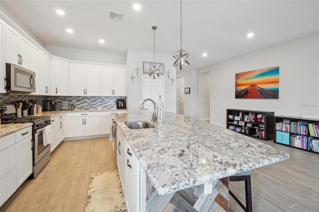 kitchen with sink, white cabinetry, decorative light fixtures, a center island with sink, and stainless steel appliances