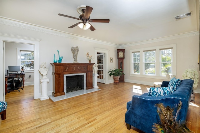 living room featuring crown molding, ceiling fan, a premium fireplace, and light hardwood / wood-style flooring