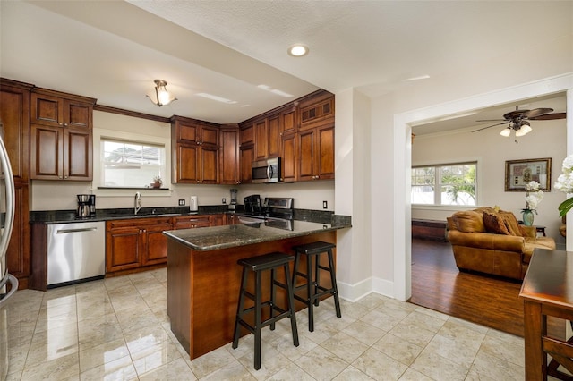 kitchen featuring sink, dark stone countertops, appliances with stainless steel finishes, a kitchen breakfast bar, and kitchen peninsula