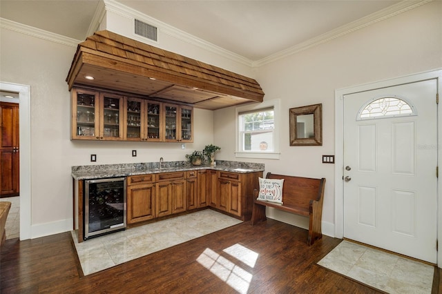 bar with wine cooler, light stone countertops, ornamental molding, and light wood-type flooring