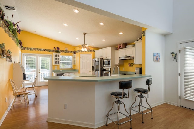 kitchen featuring a breakfast bar, white cabinetry, kitchen peninsula, stainless steel appliances, and light hardwood / wood-style floors