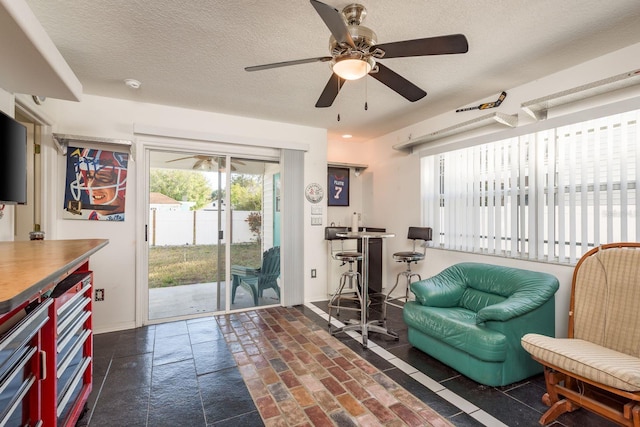 living area with ceiling fan and a textured ceiling