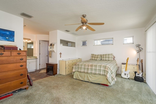 bedroom with ceiling fan, ensuite bath, carpet floors, and a textured ceiling