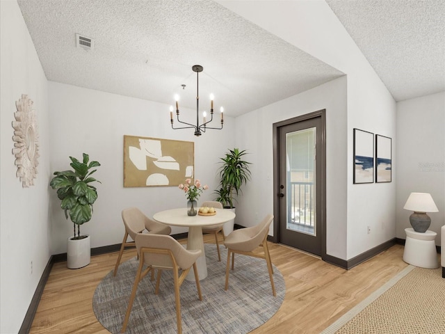 dining space with a textured ceiling, a chandelier, and light hardwood / wood-style flooring