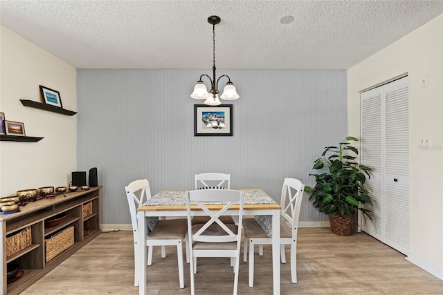 dining area featuring an inviting chandelier, light hardwood / wood-style flooring, and a textured ceiling