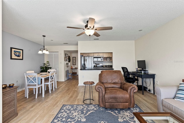 living room with ceiling fan with notable chandelier, a textured ceiling, and light wood-type flooring