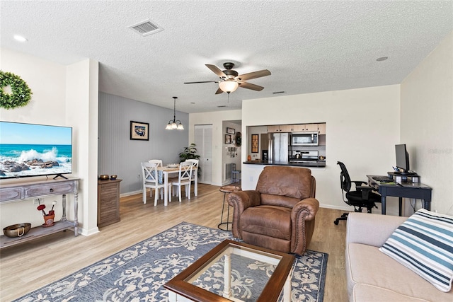 living room featuring ceiling fan with notable chandelier, a textured ceiling, and light wood-type flooring