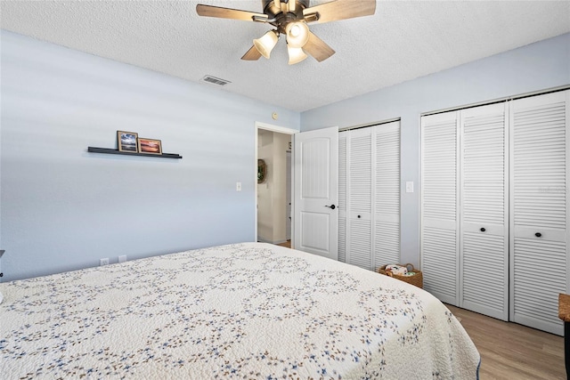 bedroom featuring ceiling fan, light wood-type flooring, a textured ceiling, and two closets