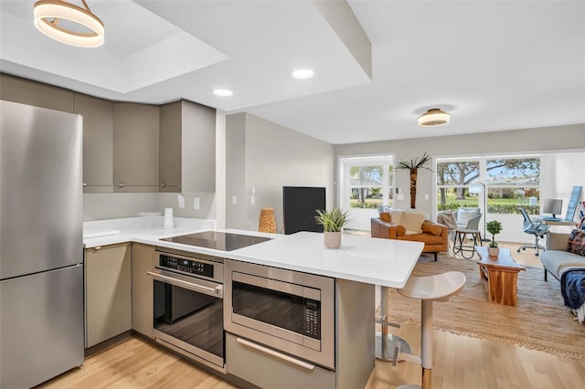 kitchen with appliances with stainless steel finishes, a breakfast bar, open floor plan, a peninsula, and light countertops