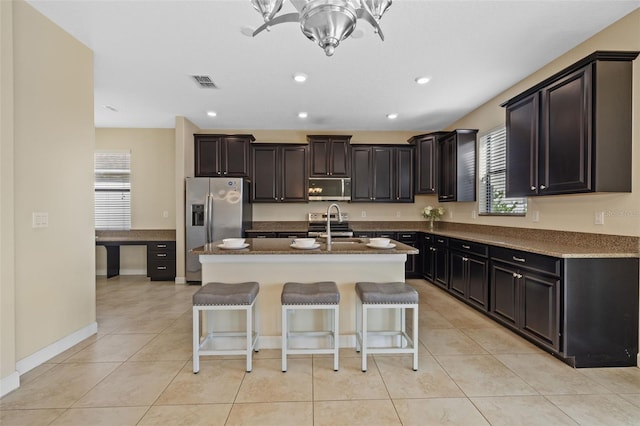 kitchen featuring light tile patterned flooring, appliances with stainless steel finishes, a breakfast bar area, and a center island with sink