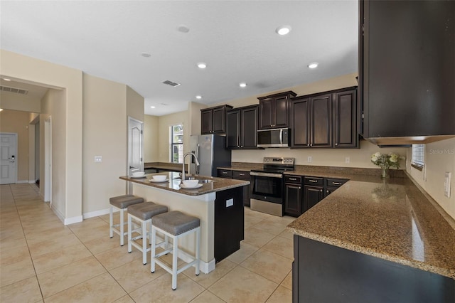 kitchen with a breakfast bar, dark stone countertops, a kitchen island with sink, light tile patterned floors, and stainless steel appliances