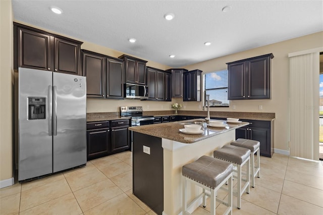 kitchen featuring a breakfast bar area, stainless steel appliances, a center island, a textured ceiling, and light tile patterned flooring