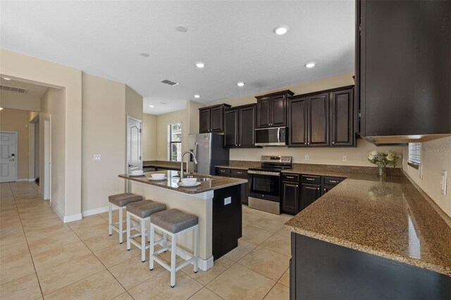 19429 Paddock View Dr, Tampa, FL 33647 - kitchen with appliances with stainless steel finishes, a breakfast bar, a center island with sink, dark stone countertops, and recessed lighting
