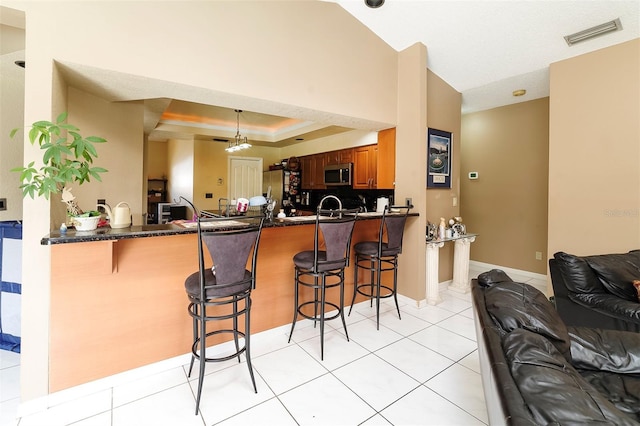 kitchen with a breakfast bar area, light tile patterned floors, a tray ceiling, kitchen peninsula, and stainless steel appliances