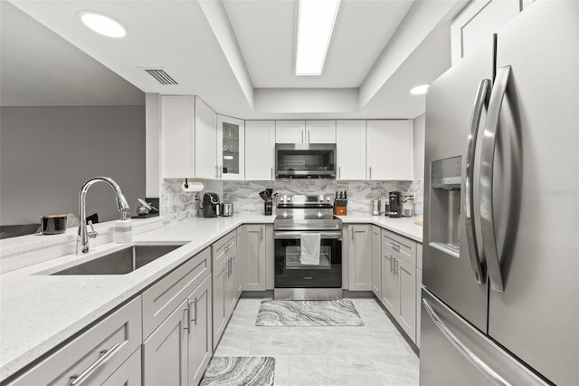 kitchen featuring sink, stainless steel appliances, light stone counters, decorative backsplash, and a raised ceiling